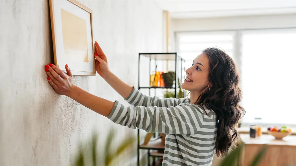 Frau hängt ein Bild an eine helle Wand