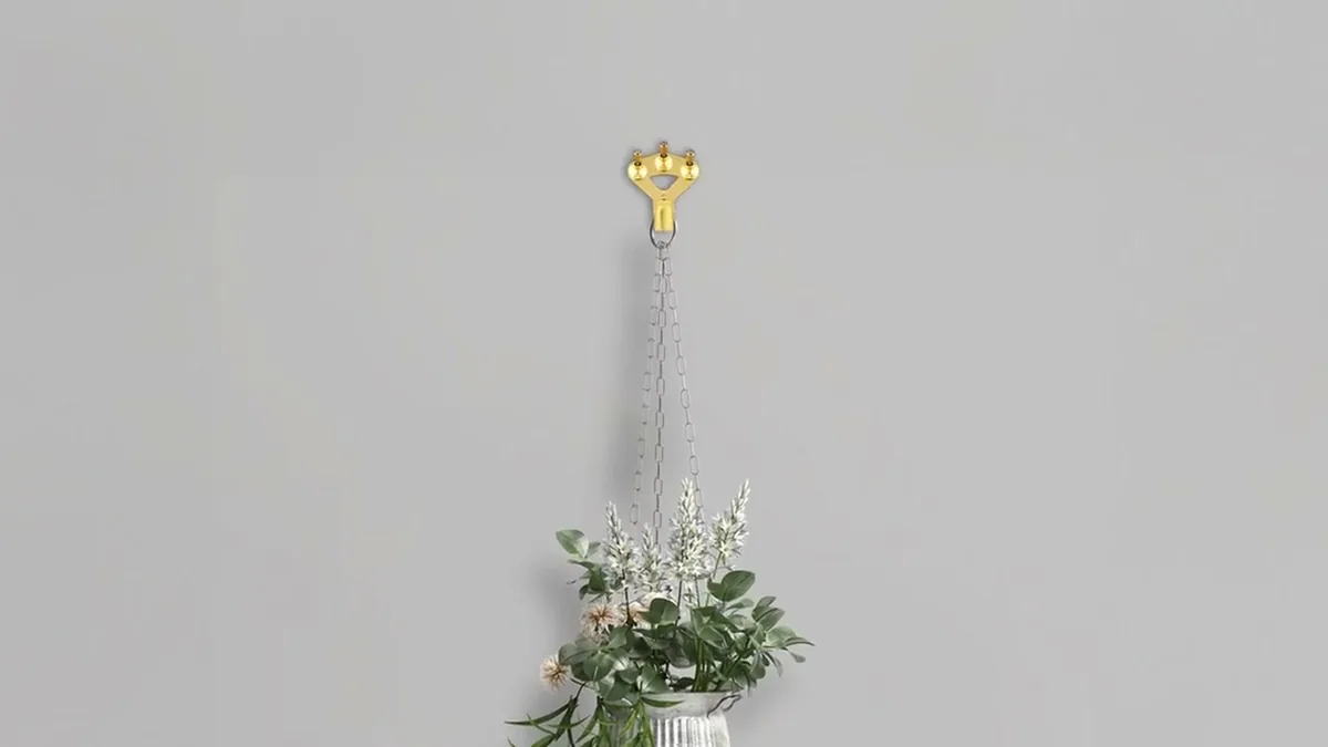 Hängende Pflanze in weißem Topf an einem goldenen FLOREAT-Haken vor grauer Wand