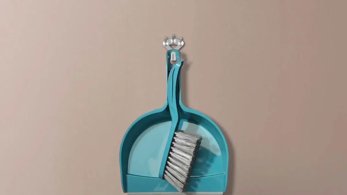 Türkise Kehrschaufel mit Besen hängt an einem FLOREAT-Haken vor rosafarbener Wand