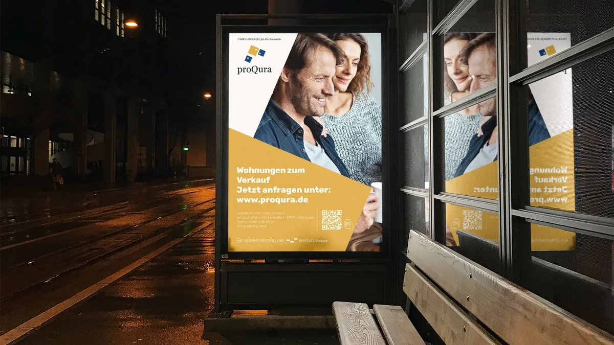 Goldenes Plakat der proQura in einer beleuchteten Haltestelle bei Nacht.