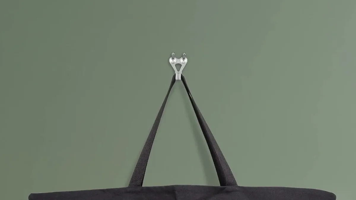 Schwarze Tasche hängt an einem silbernen FLOREAT-Haken vor grüner Wand