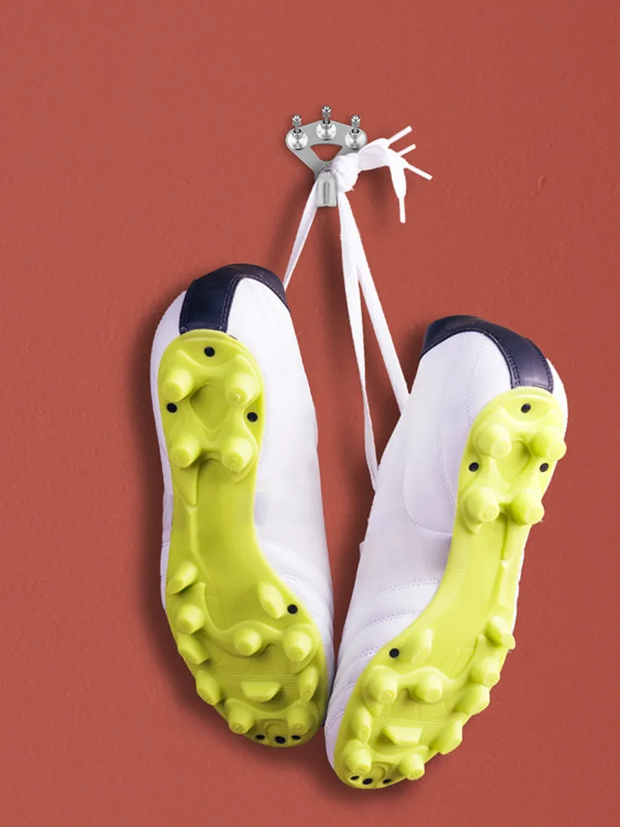 Fußballschuhe mit gelben Stollen hängen an einem silbernen FLOREAT-Haken vor roter Wand