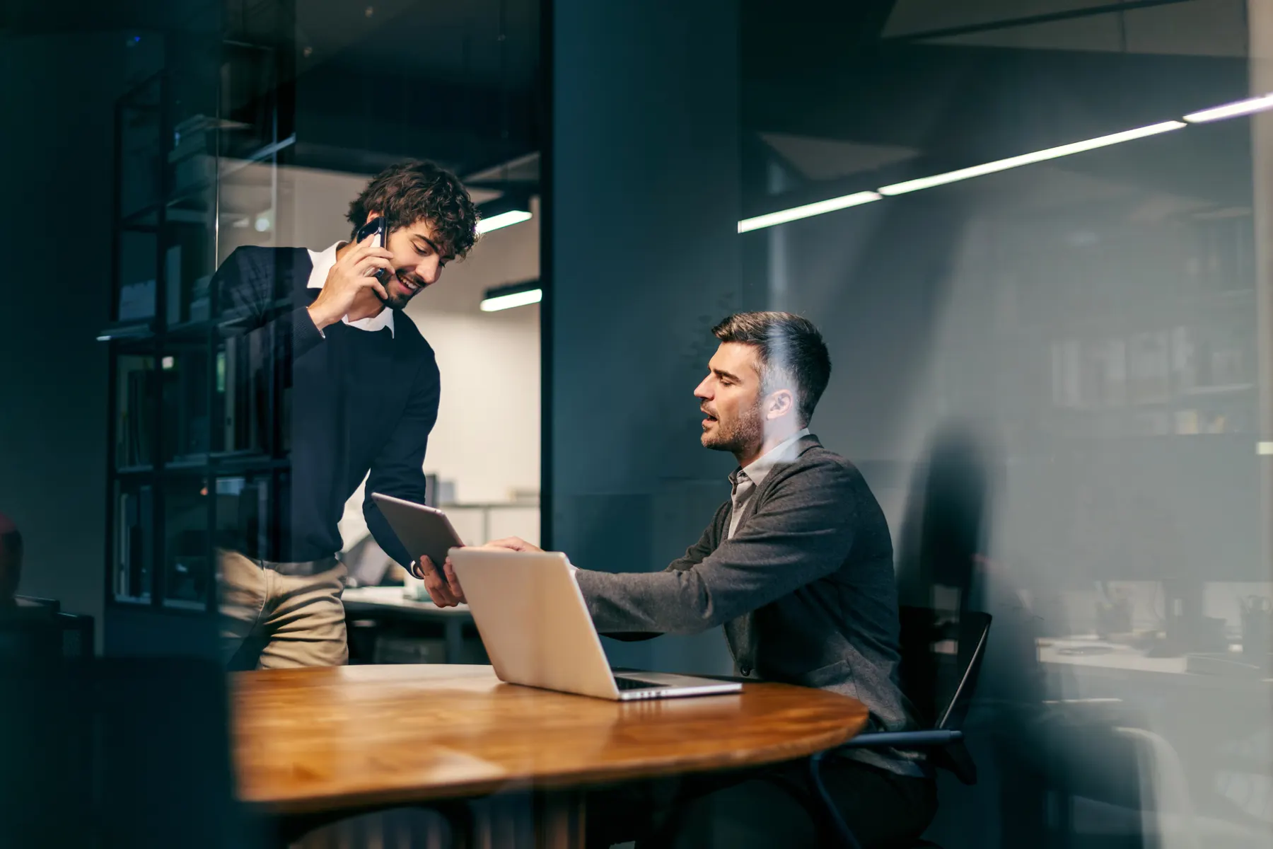 Zwei Kollegen im Büro, einer am Telefon, einer am Laptop